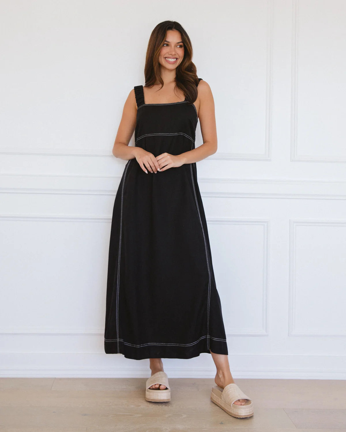 Woman wearing a black dress standing against a white paneled wall.